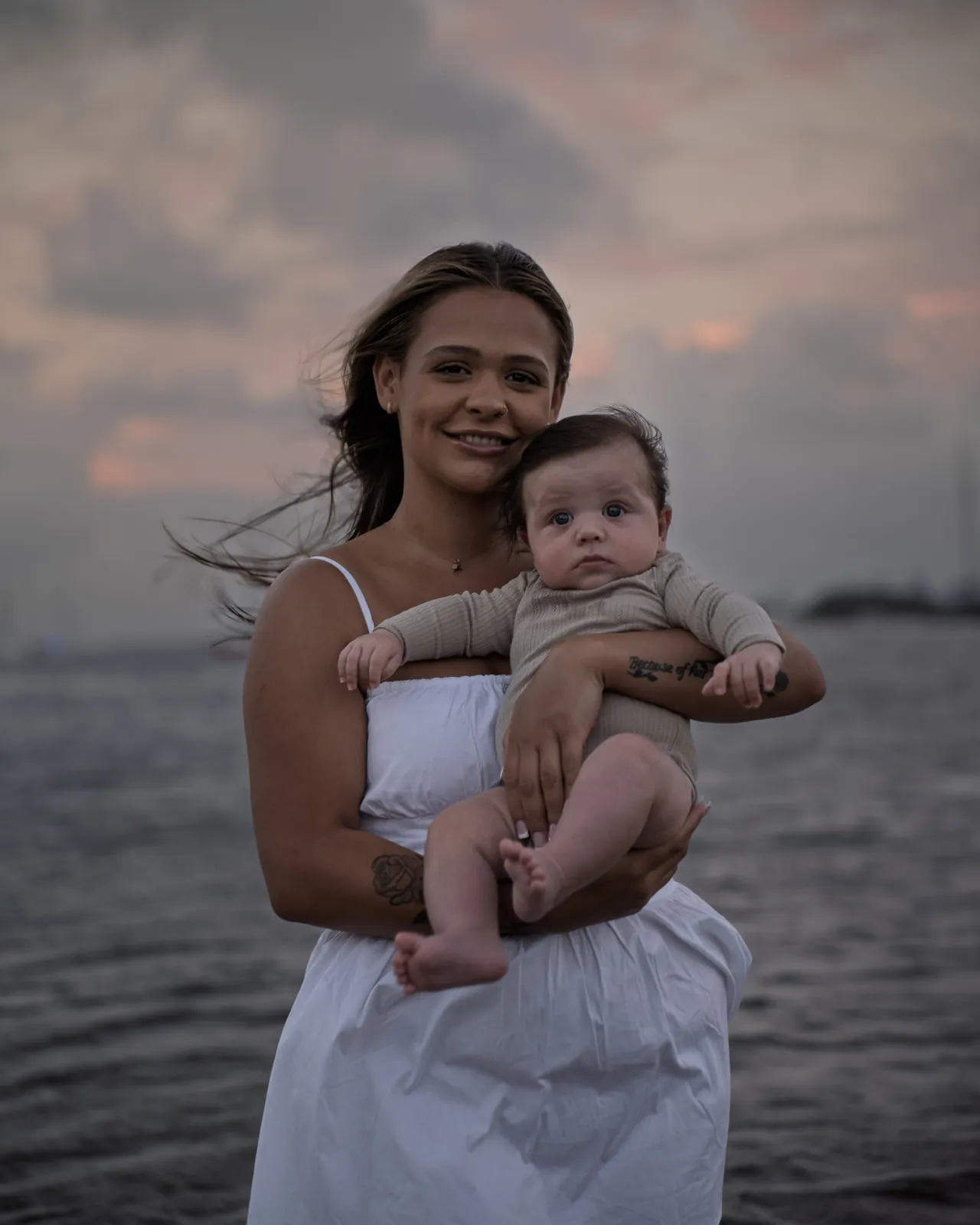 A mother holding her baby up at the water at dusk