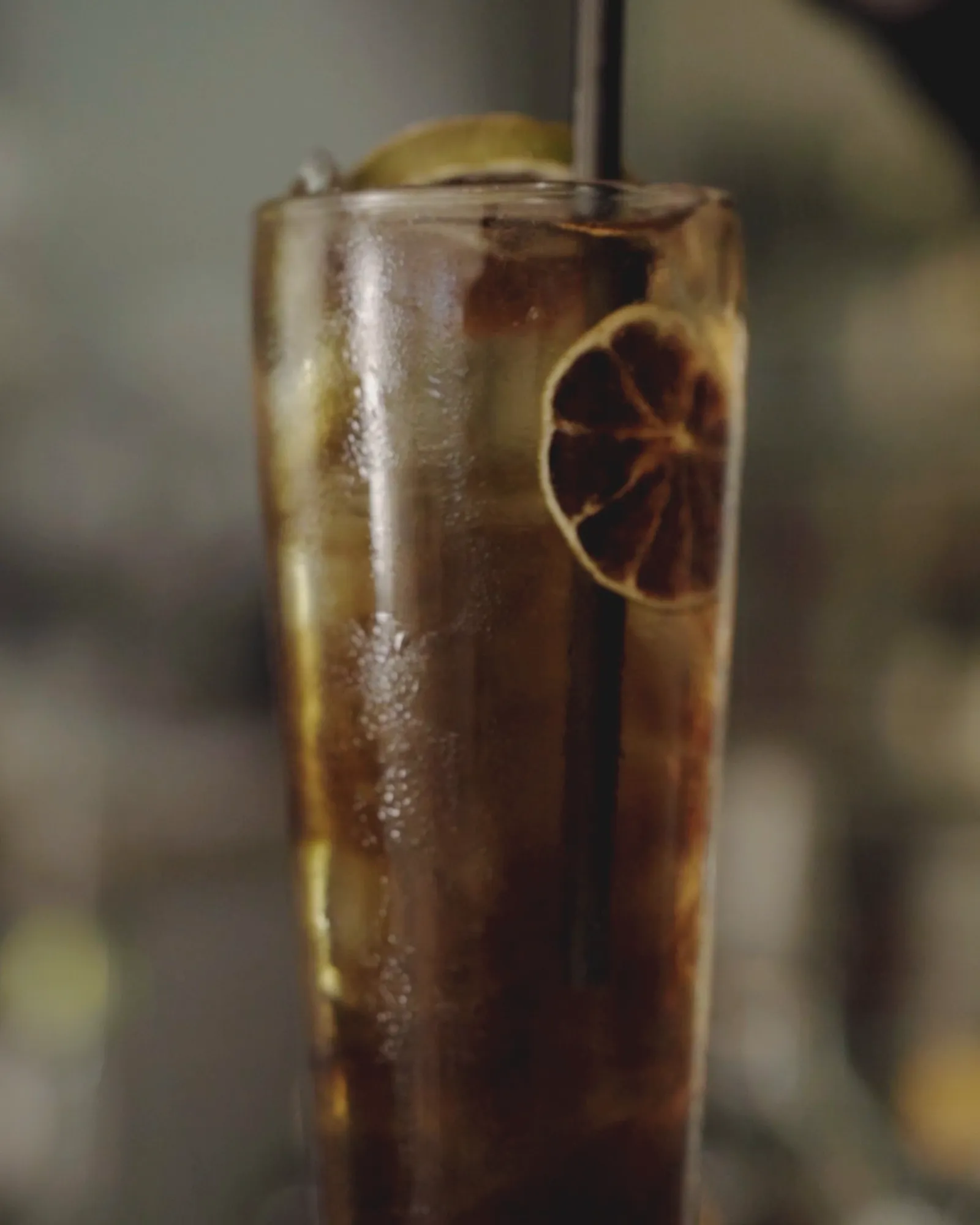 A tall iced cocktail with a dried lemon wheel on the bar