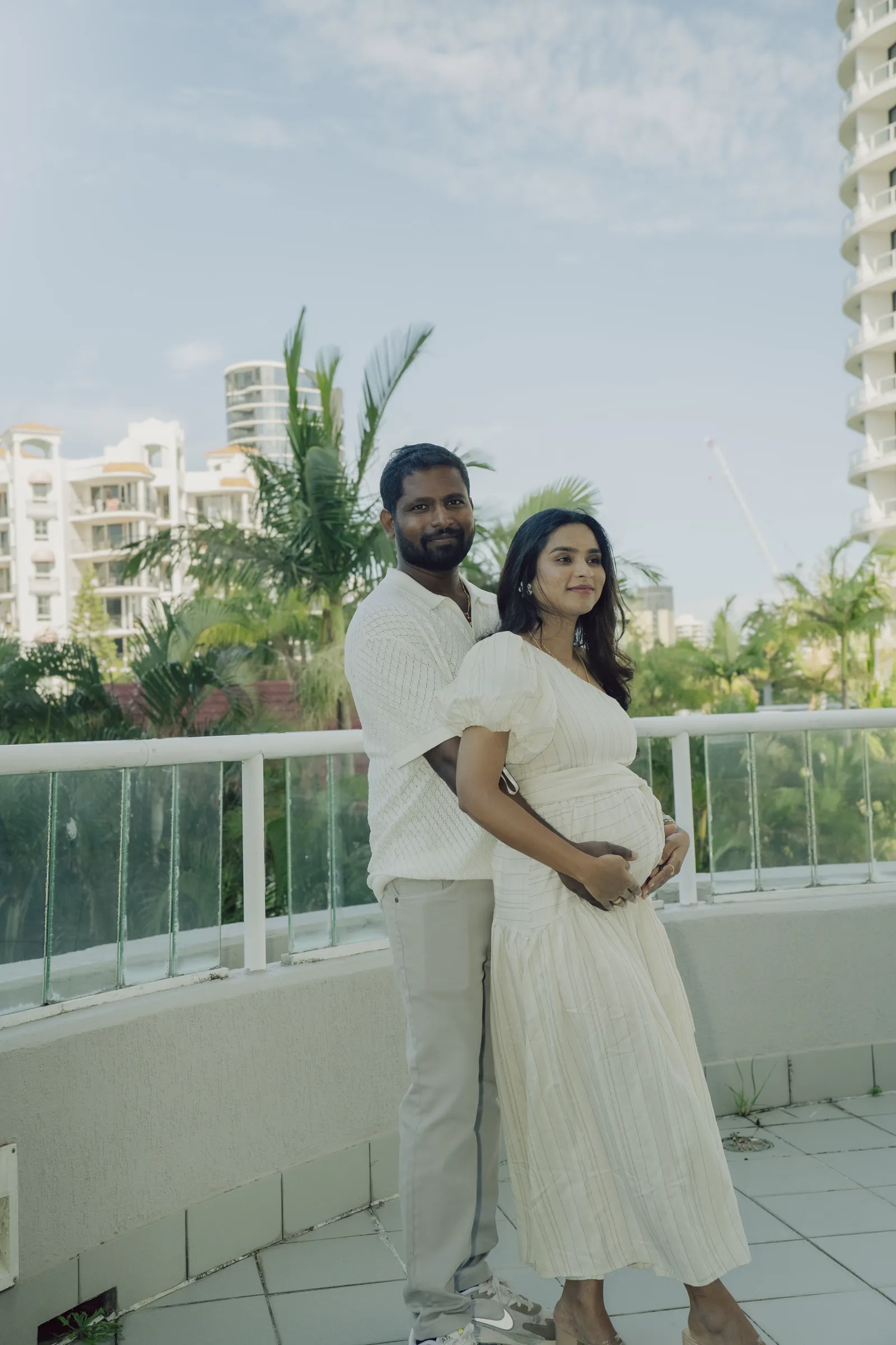 An expecting couple looking out over the balcony rail, backs to camera