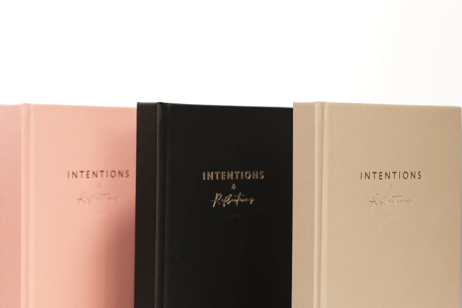 Rose, black and sand Intentions journals lined up on white