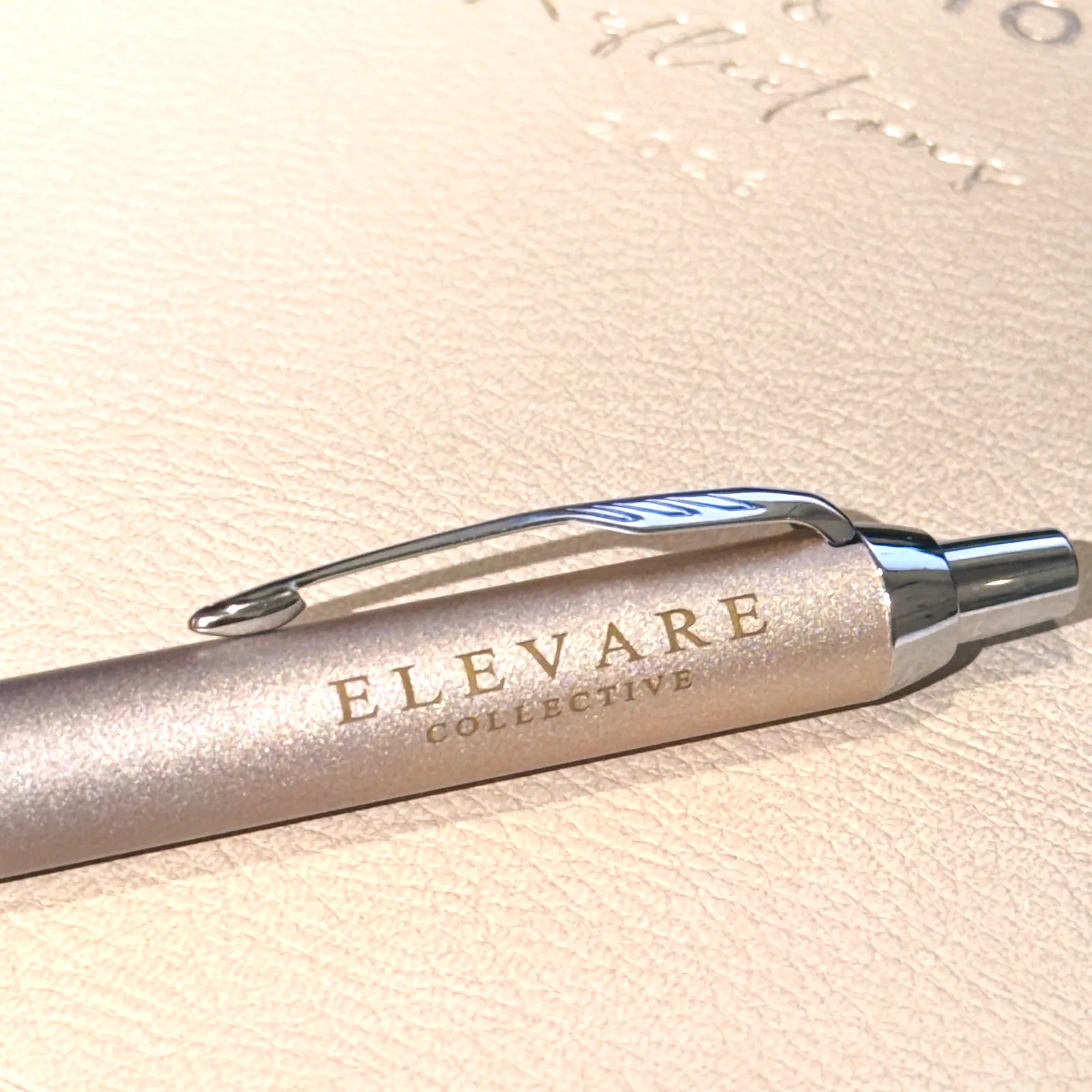 Macro of a debossed journal cover with an Elevare Collective pen resting on it