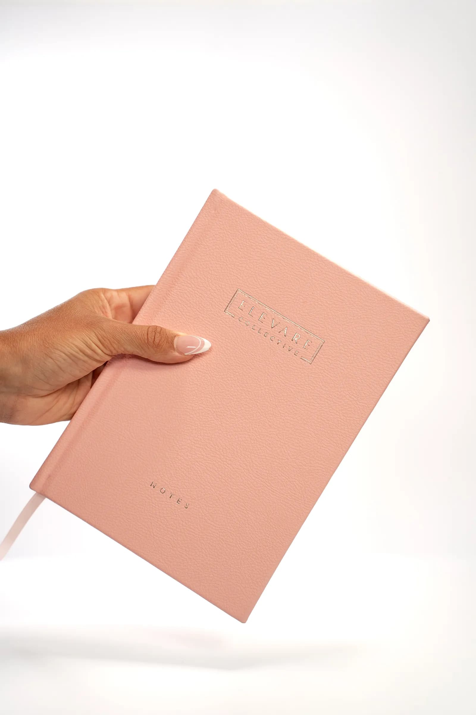 A hand holding a rose Elevare journal against a white background