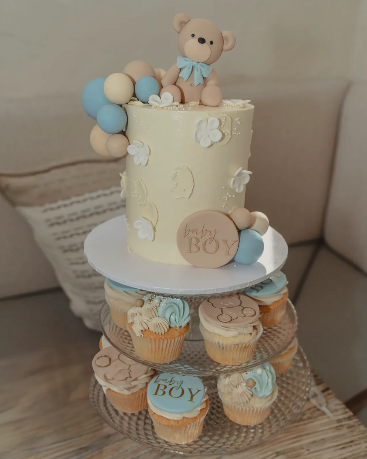 A teddy bear christening cake and cupcakes on a styled dessert table