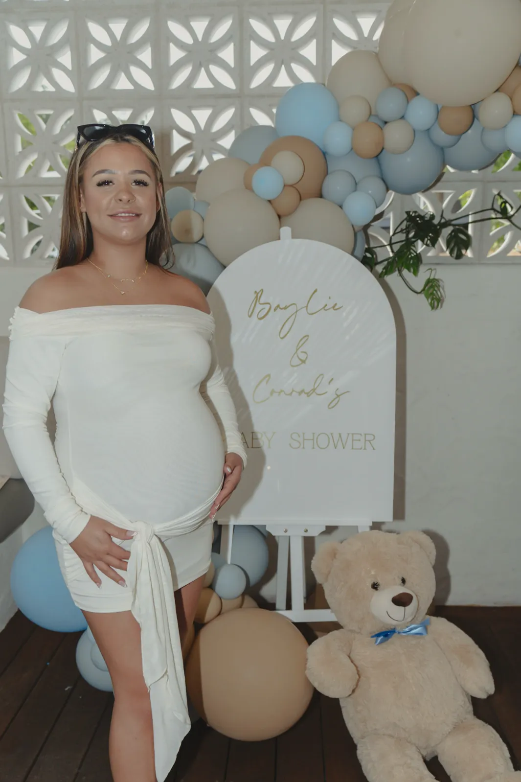 The mum to be standing in front of a blue and beige balloon arch