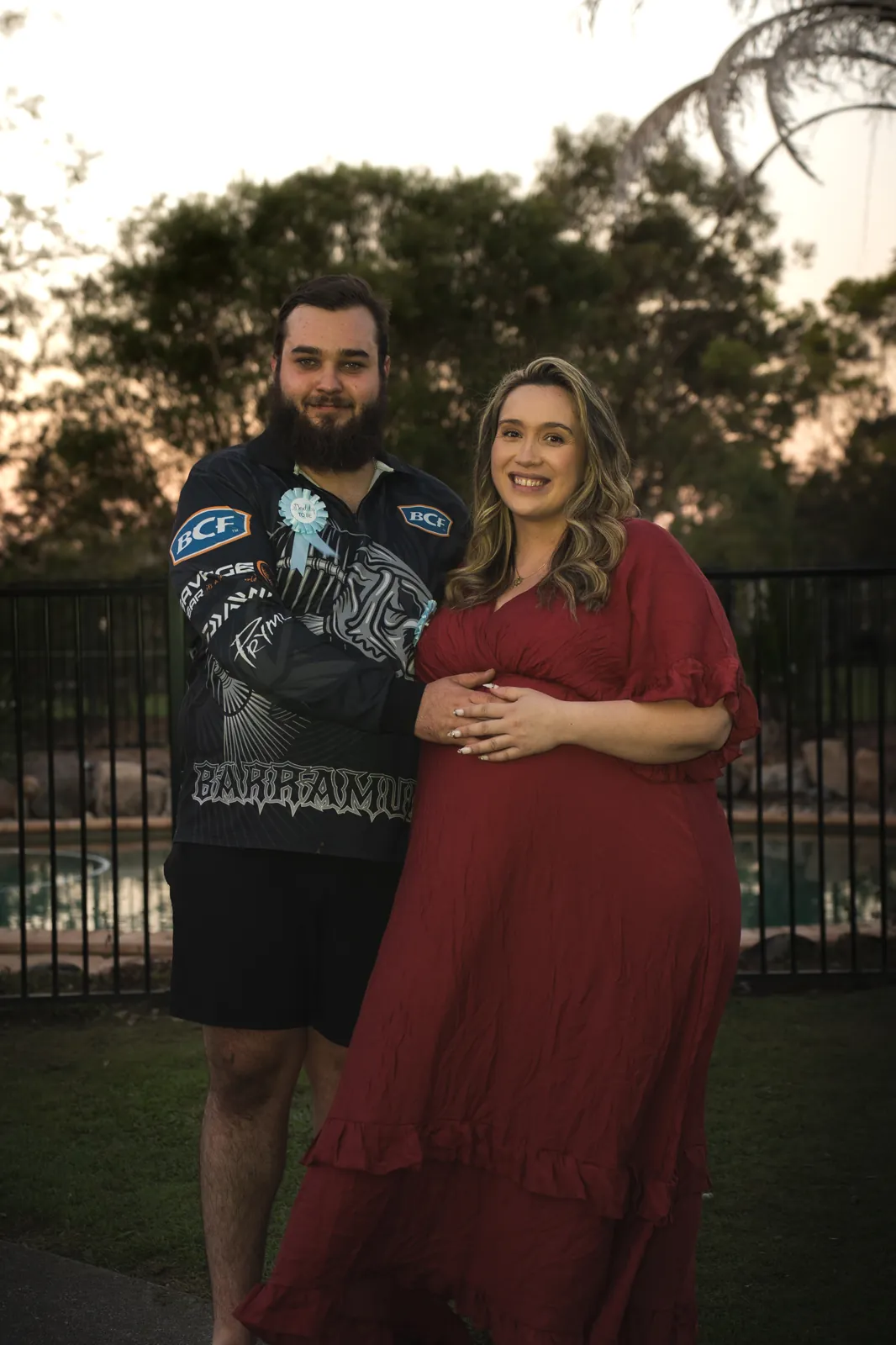 An expecting couple standing together in the backyard at dusk
