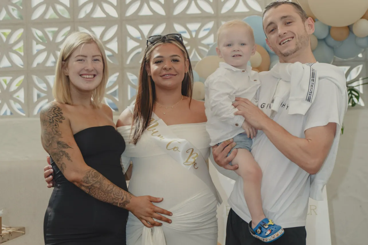 Three guests and a toddler in front of the balloon wall